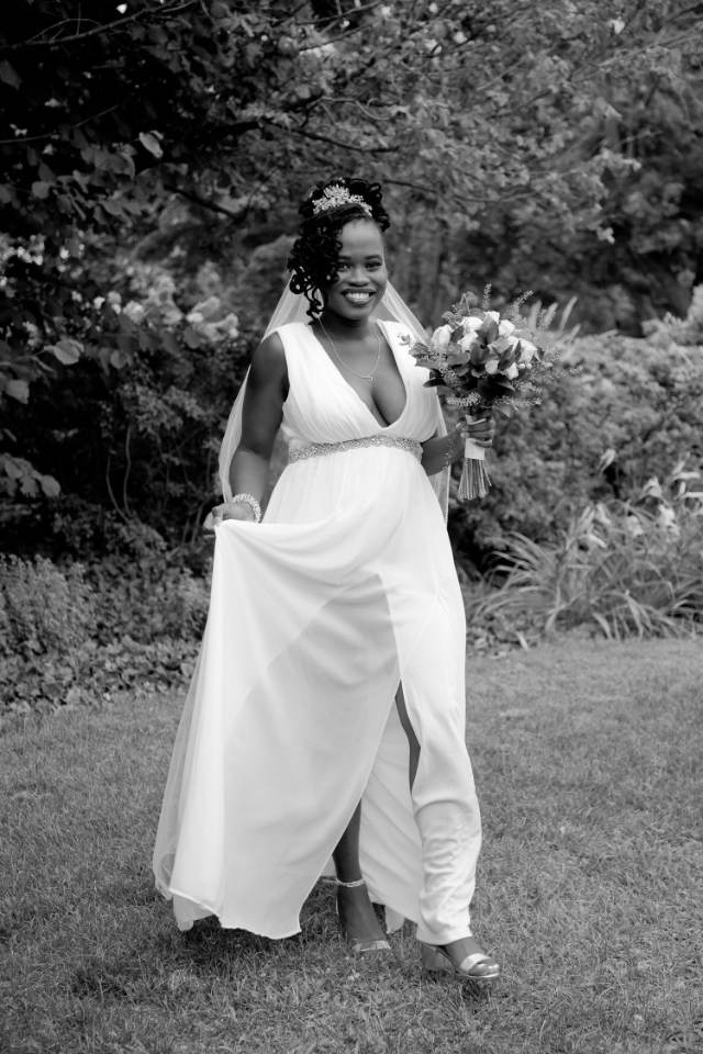 Bride walking across a lawn in a flowing gown, black and white